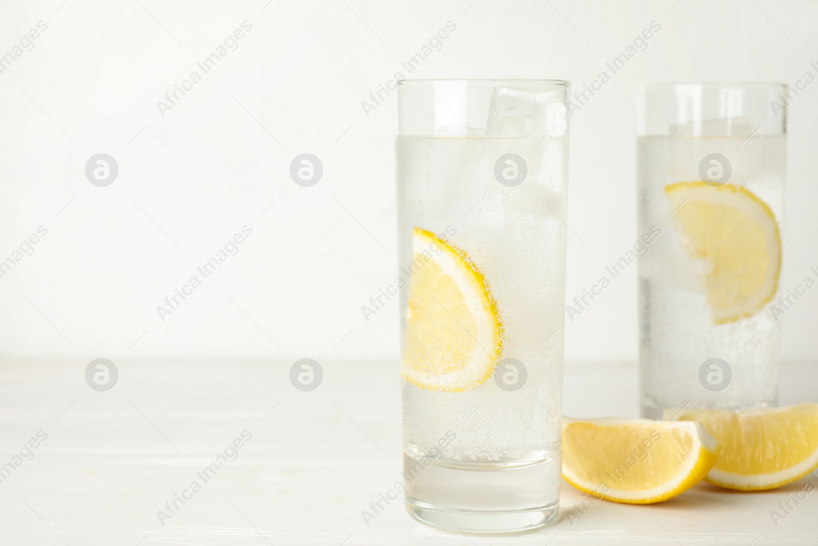 Photo of Soda water with lemon slices and ice cubes on white wooden table. Space for text