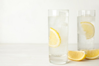 Soda water with lemon slices and ice cubes on white wooden table. Space for text