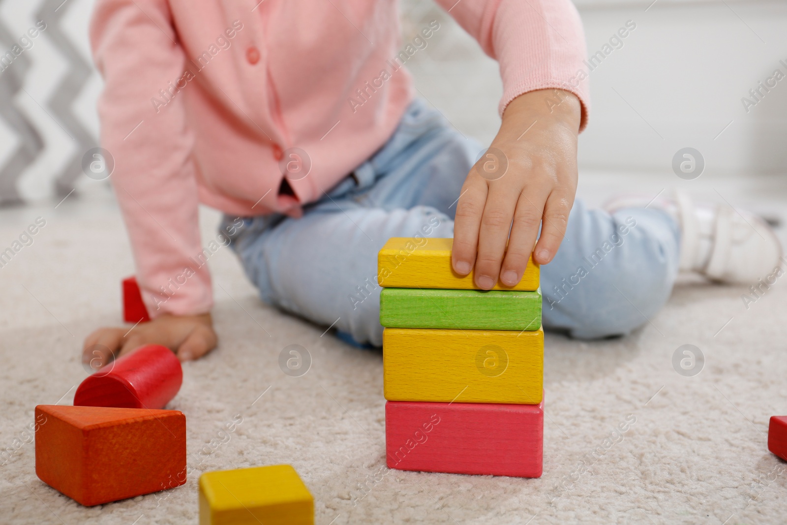Photo of Cute little girl playing with colorful building blocks indoors, closeup