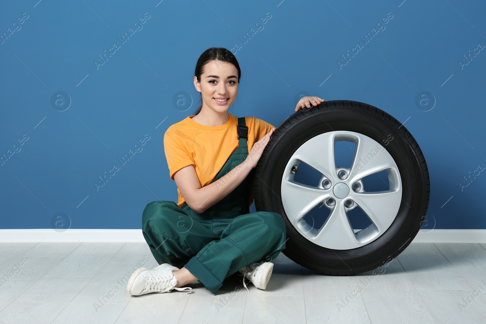 Photo of Female mechanic in uniform with car tire on color wall background