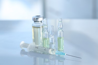 Glass vial, ampoules and syringe on white table, closeup