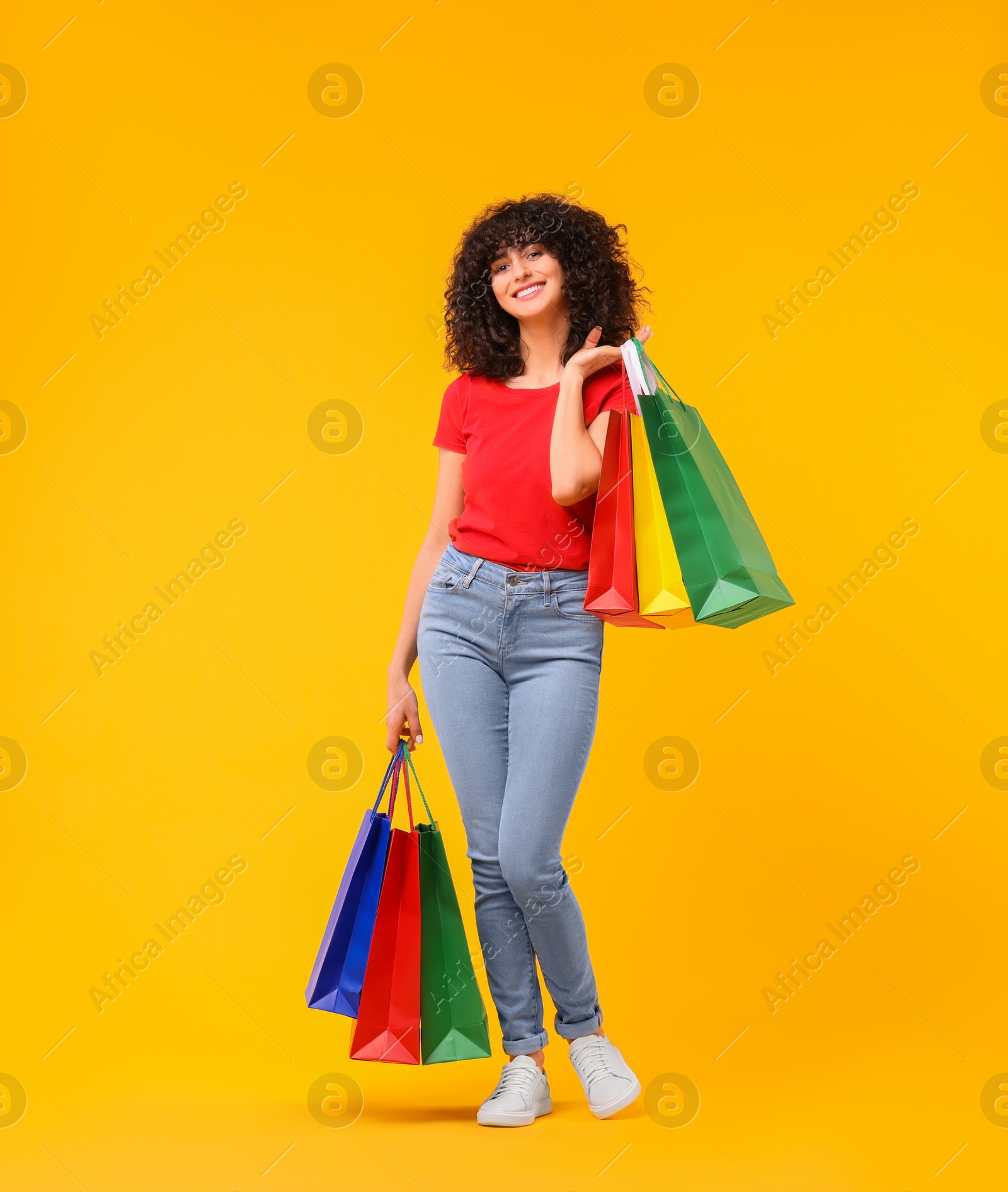 Photo of Happy young woman with shopping bags on yellow background