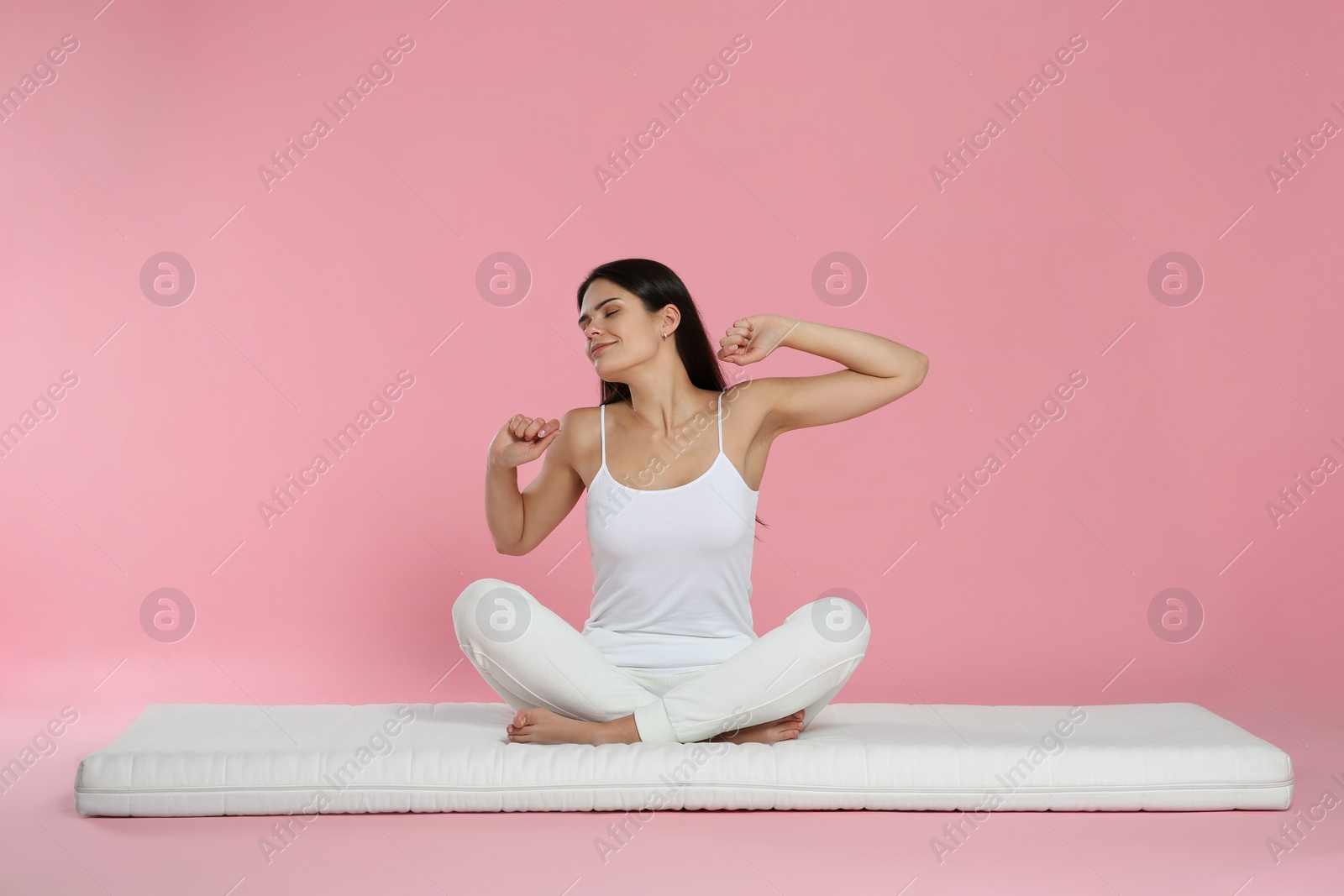 Photo of Young woman stretching on soft mattress against pink background