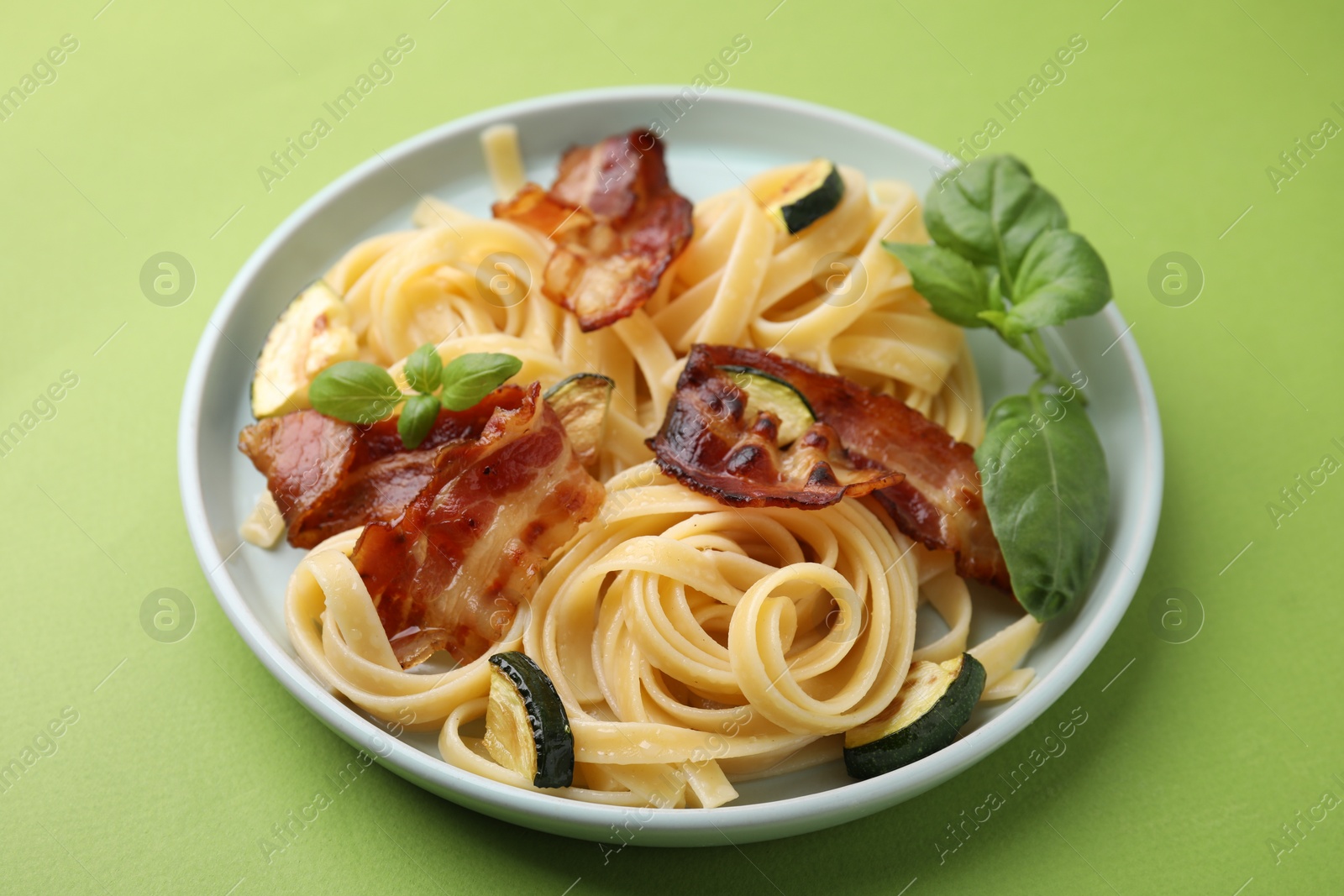 Photo of Tasty pasta with bacon and basil on light green table