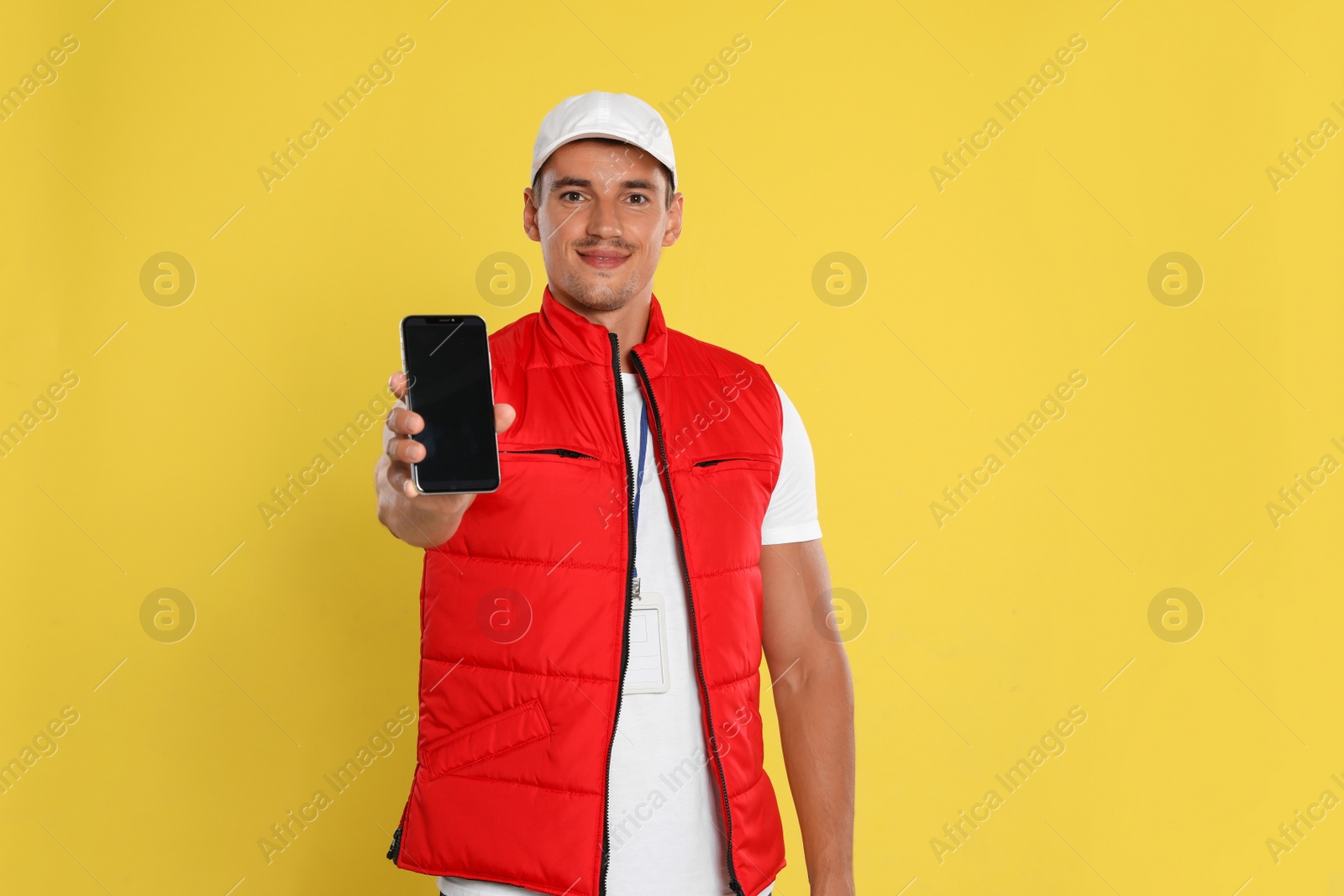 Photo of Happy young courier with mobile phone on yellow background