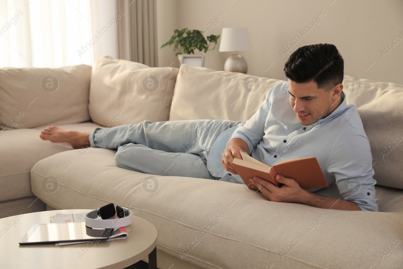 Photo of Man reading book on sofa in living room