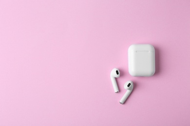 Photo of Modern wireless earphones and charging case on pink background, flat lay. Space for text