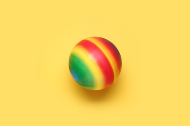 Bright rubber kids' ball on pale yellow background, top view