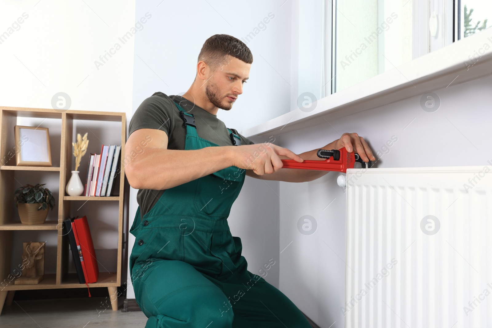 Photo of Professional plumber using adjustable wrench for installing new heating radiator in room