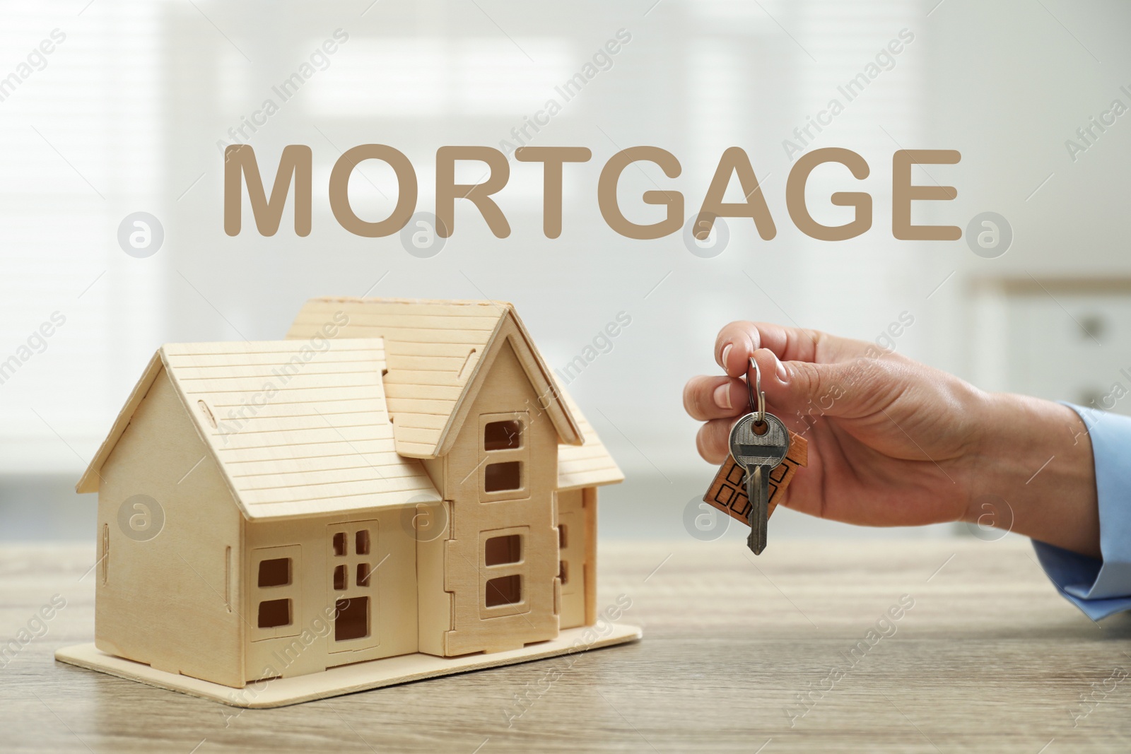 Image of Mortgage concept. Real estate agent with house model and key at wooden table, closeup