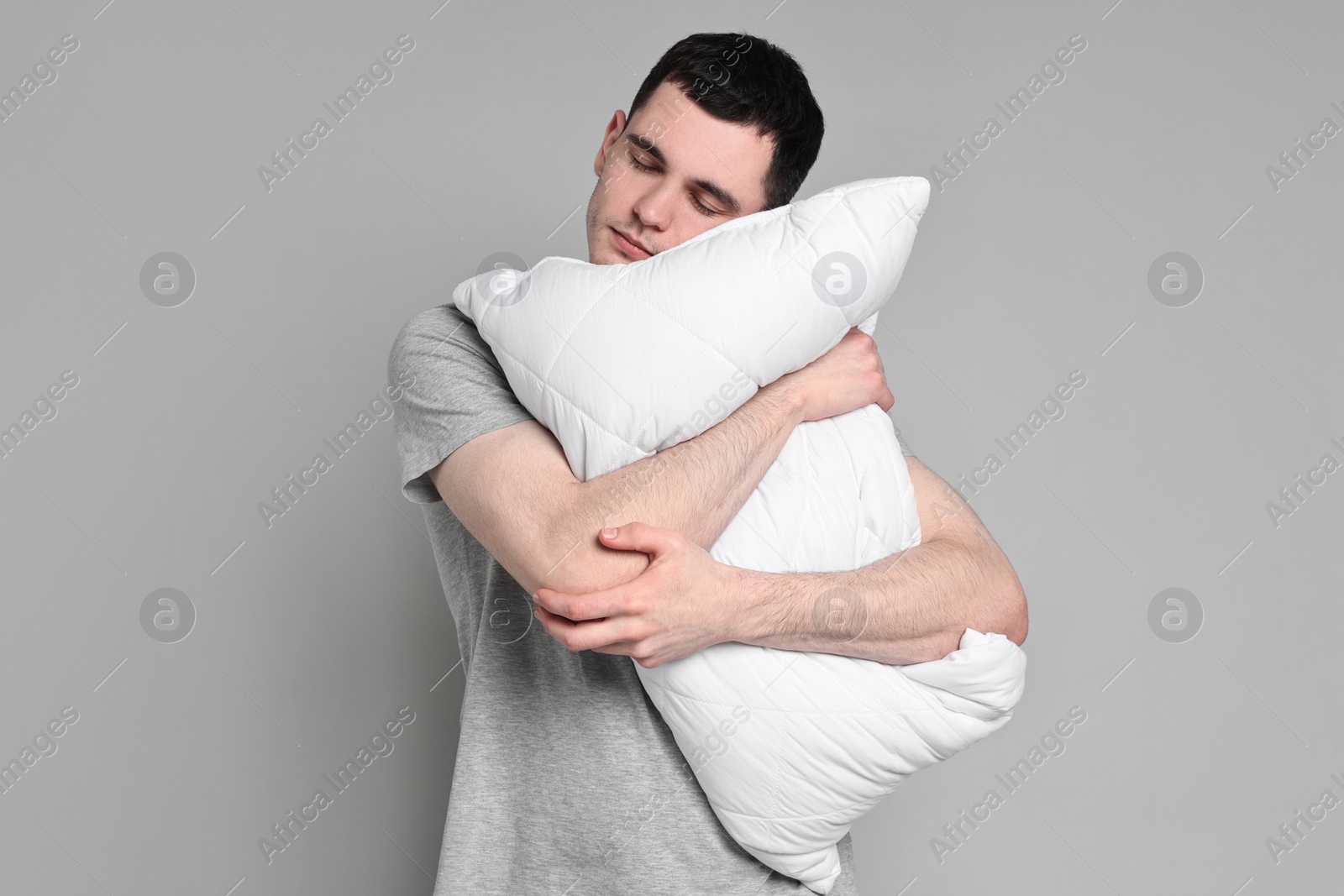 Photo of Man in pyjama holding pillow and sleeping on grey background