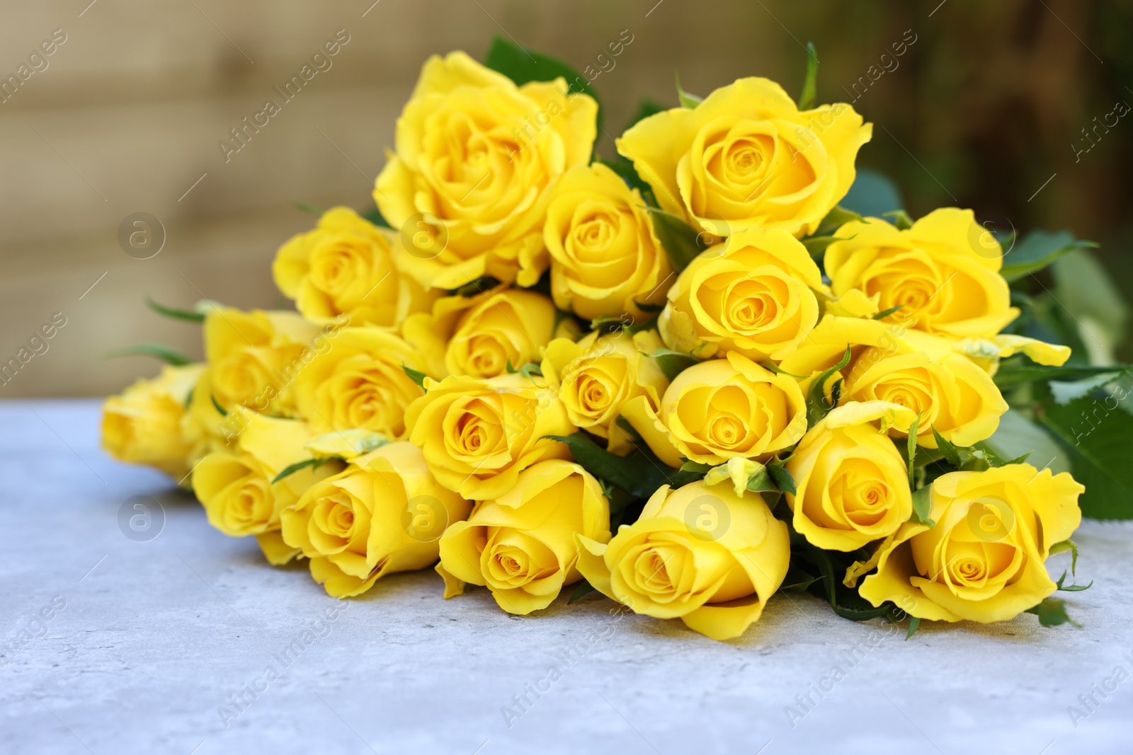 Photo of Beautiful bouquet of yellow roses on light table outdoors