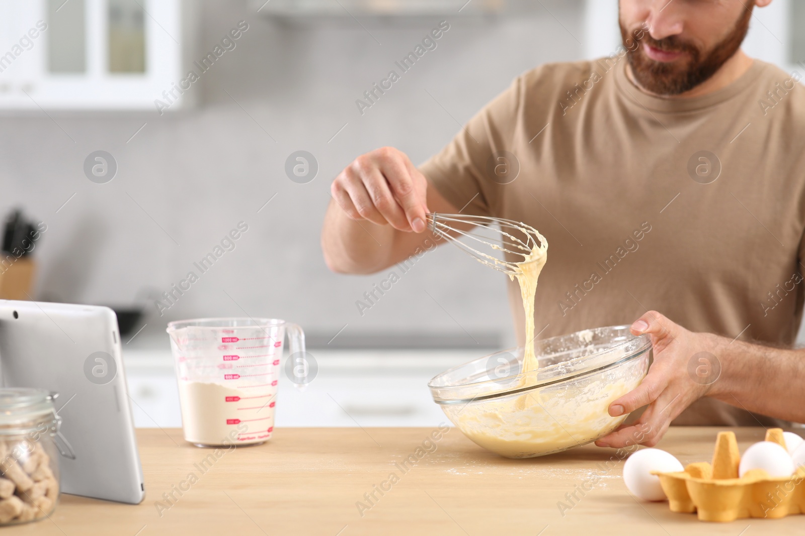 Photo of Man making dough while watching online cooking course via tablet in kitchen, closeup