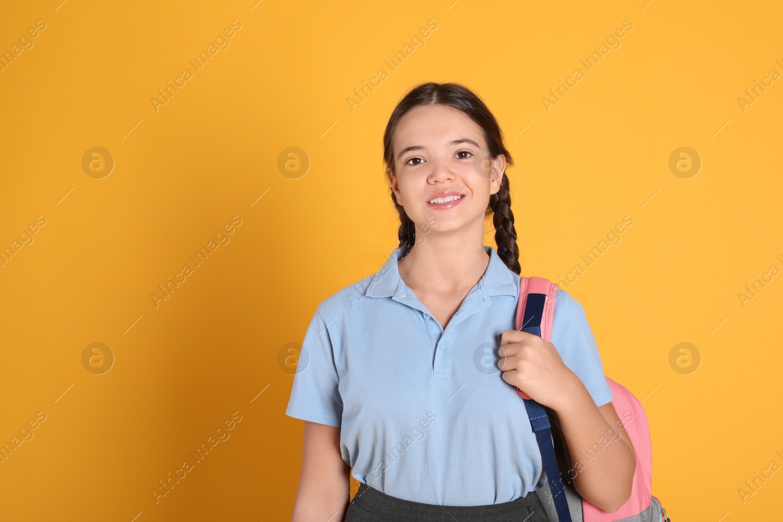 Photo of Teenage girl in school uniform with backpack on orange background, space for text