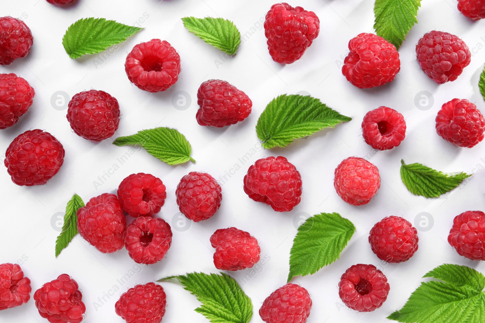 Photo of Tasty ripe raspberries and green leaves on white background, flat lay