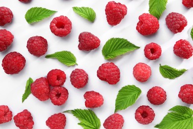 Tasty ripe raspberries and green leaves on white background, flat lay