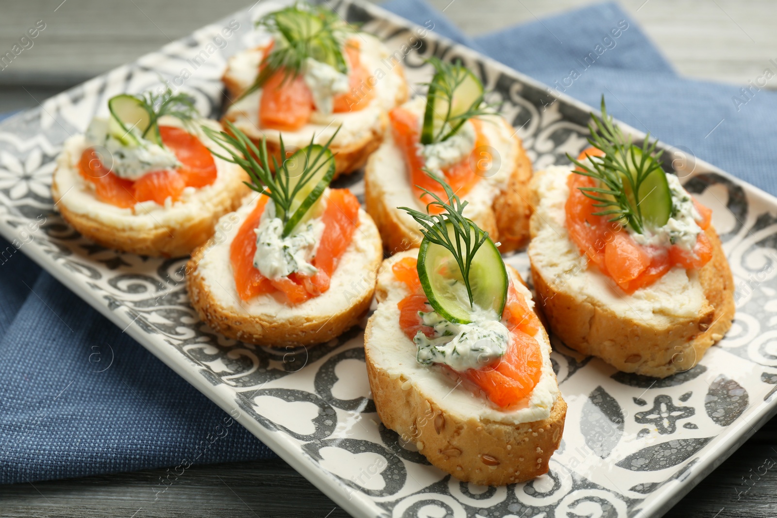 Photo of Tasty canapes with salmon, cucumber, cream cheese and dill on wooden table, closeup