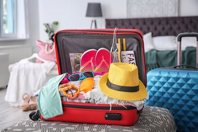 Photo of Open suitcase with different clothes and accessories for summer journey on ottoman chair