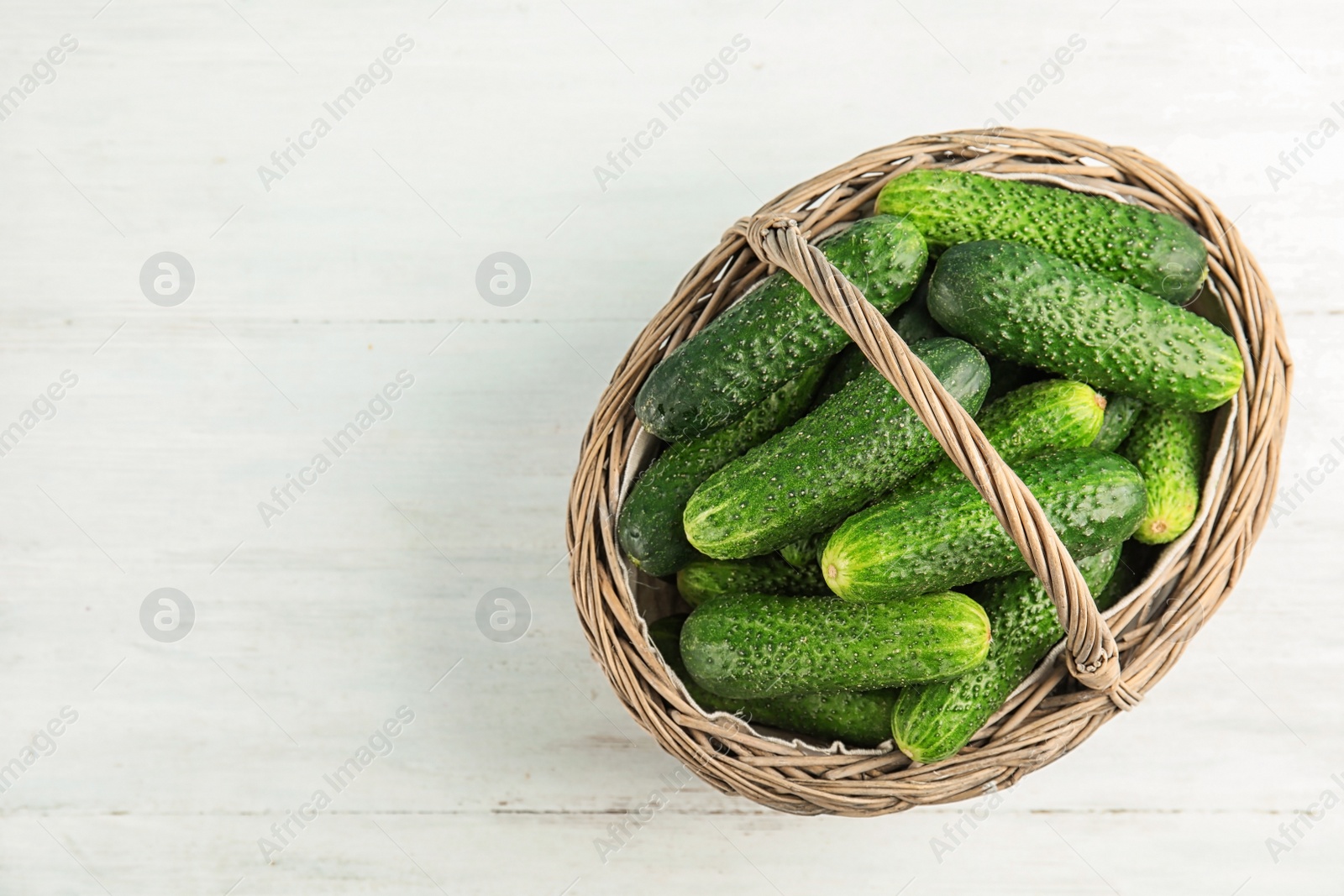 Photo of Wicker basket with ripe fresh cucumbers on table, top view