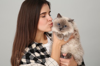 Photo of Woman kissing her cute cat on light grey background