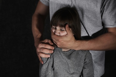 Photo of Adult man covering scared little girl's mouth, space for text. Child in danger
