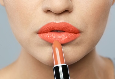 Young woman applying beautiful lipstick on gray background, closeup