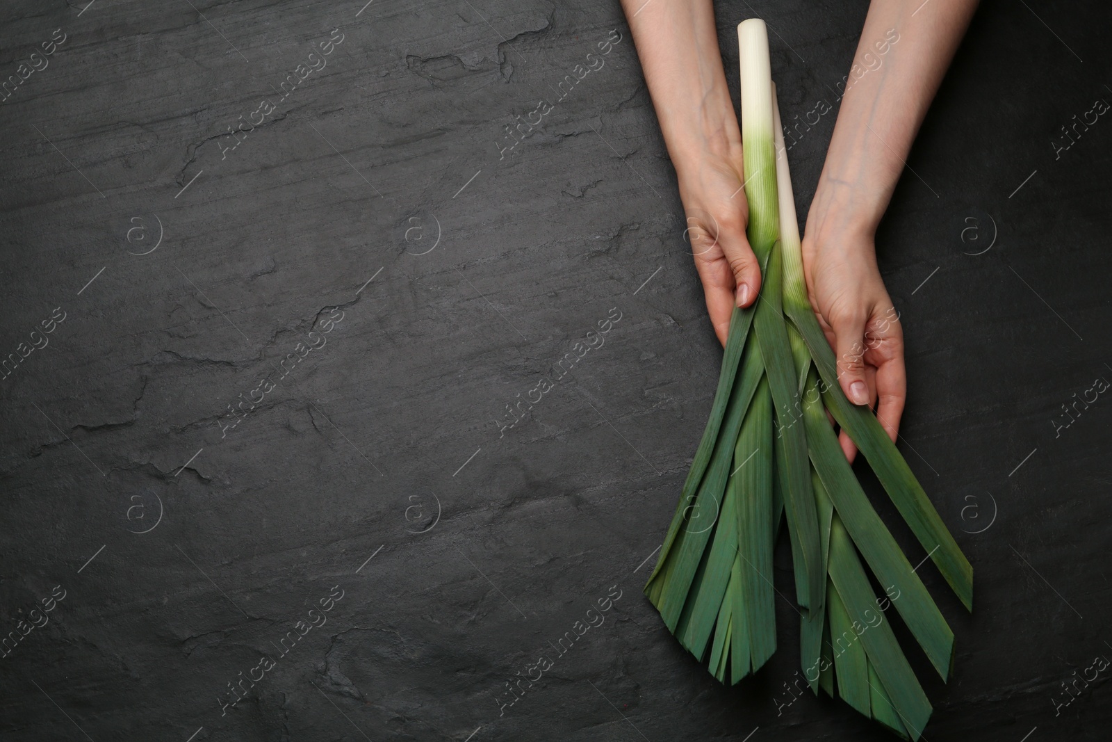 Photo of Woman with fresh raw leeks at black table, top view. Space for text