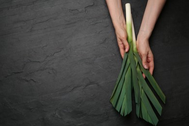 Woman with fresh raw leeks at black table, top view. Space for text