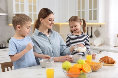 Mother and her little children having breakfast at table in kitchen