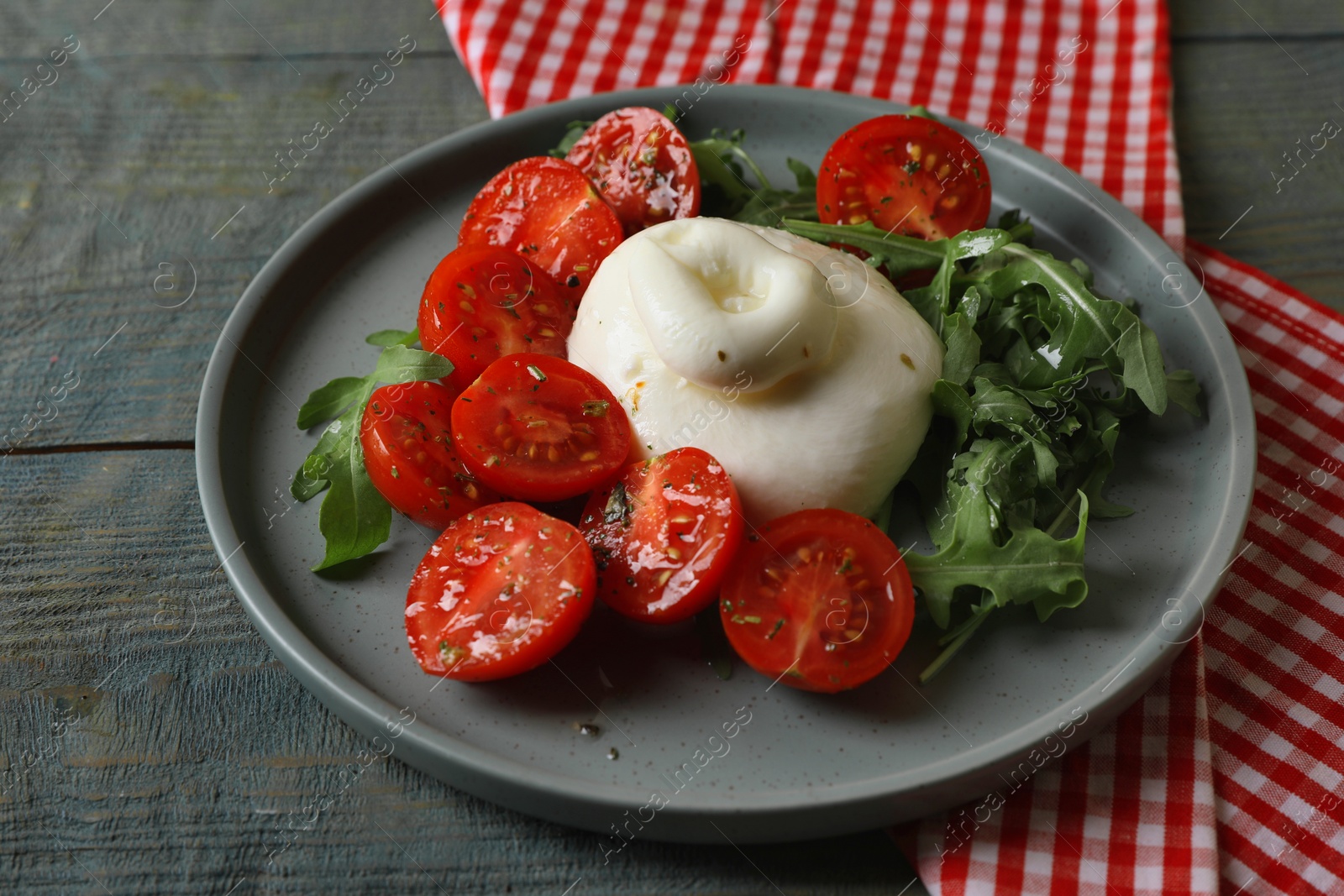 Photo of Delicious burrata cheese with tomatoes and arugula on grey wooden table, closeup