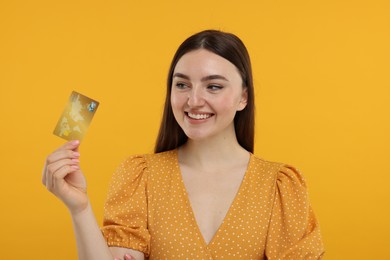 Happy woman with credit card on orange background