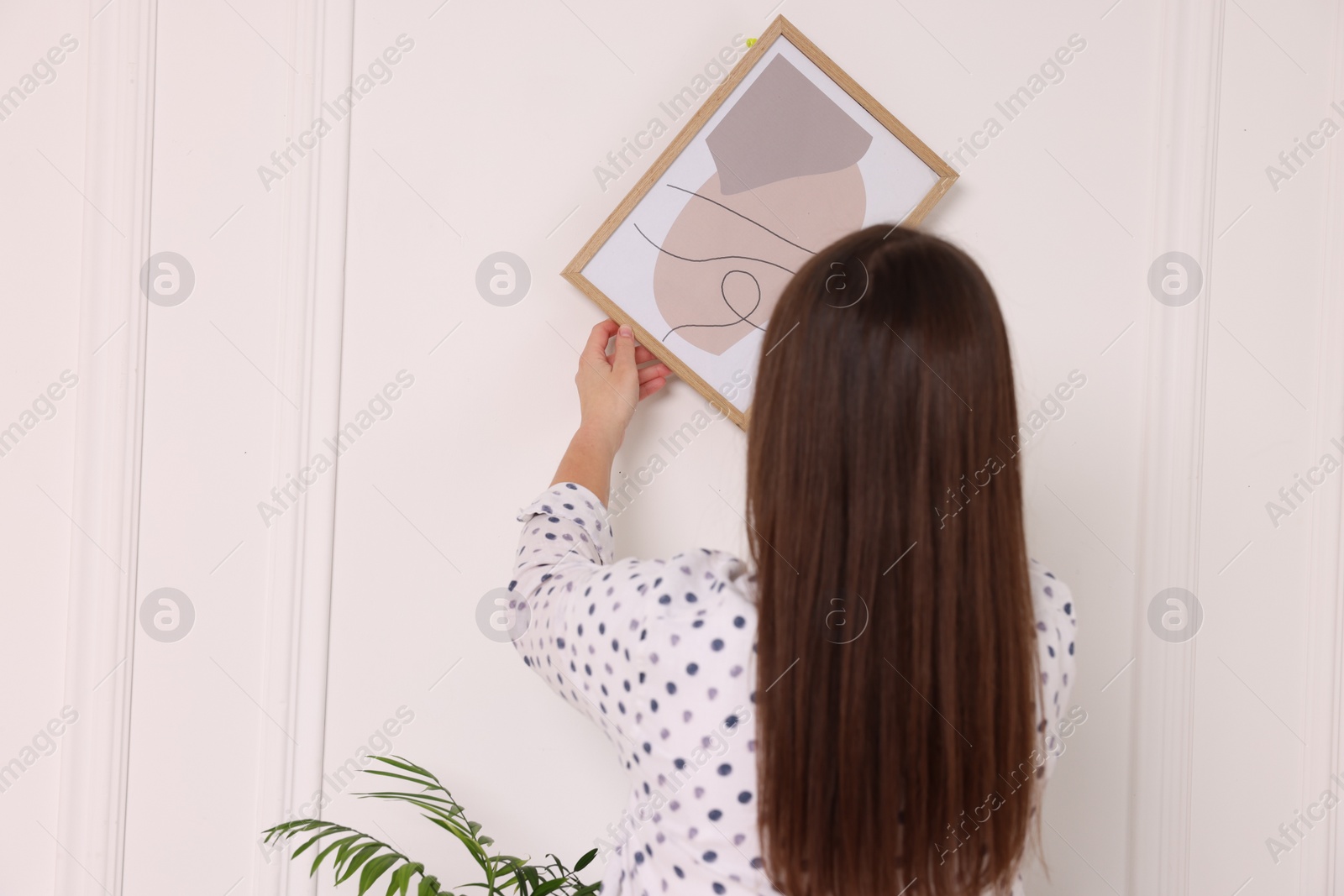 Photo of Woman hanging picture frame on white wall indoors, back view