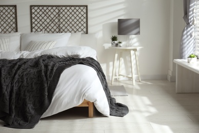 Photo of Comfortable bed with warm knitted plaid in stylish room interior