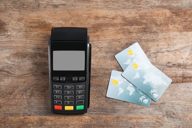 Modern payment terminal and credit cards on wooden background, top view