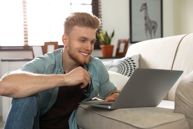 Photo of Young man using laptop in living room