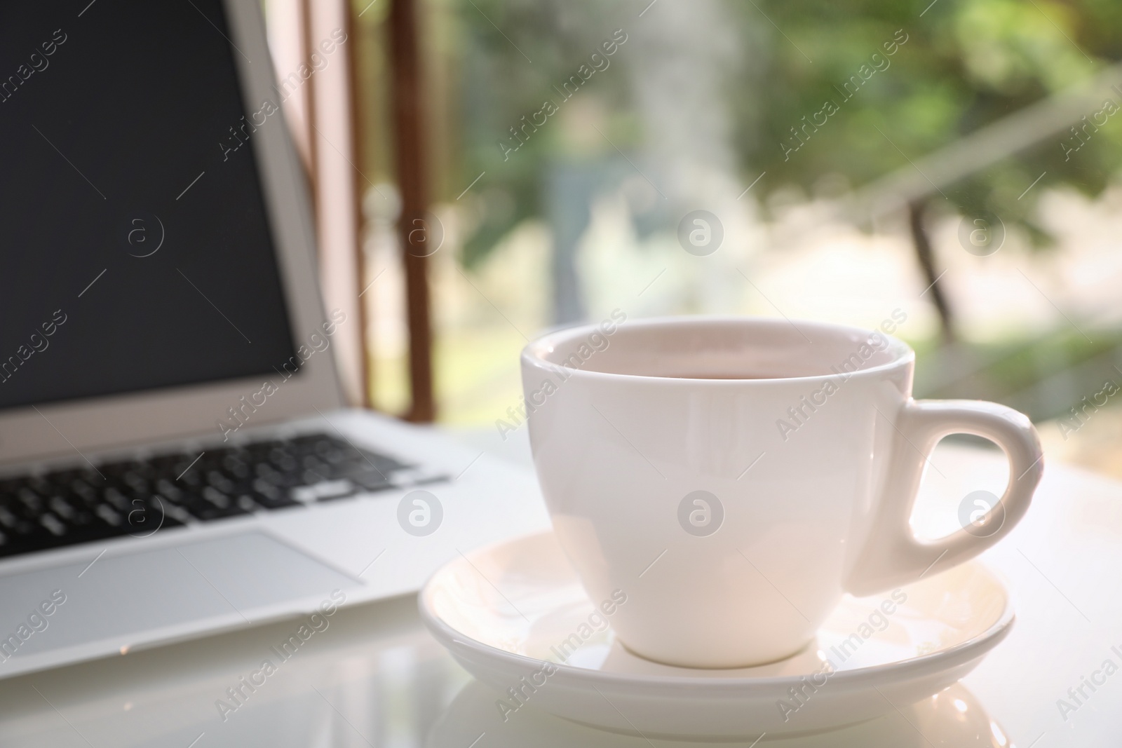 Photo of Cup of delicious morning coffee near laptop on white table