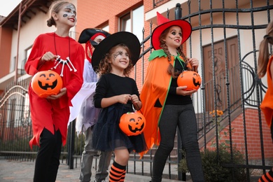 Photo of Cute little kids wearing Halloween costumes going trick-or-treating outdoors