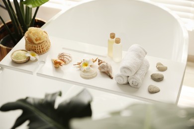 Photo of Bath tray with spa products, towels and shells on tub in bathroom