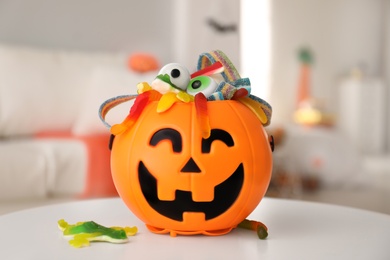 Photo of Halloween trick or treat bucket with different sweets on white table indoors