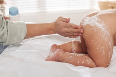 Photo of Mother applying dusting powder onto her baby on towel at home, closeup