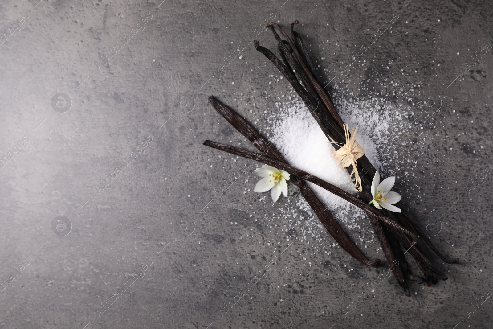 Photo of Vanilla pods, sugar and flowers on gray table, flat lay. Space for text