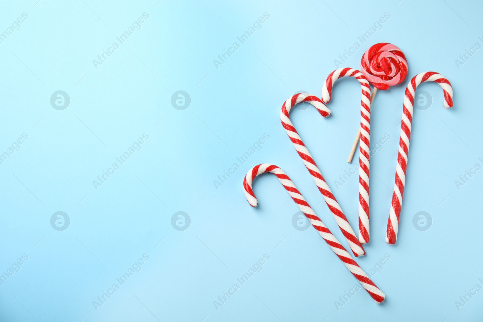 Photo of Flat lay composition with candy canes and lollipop on light blue background. Space for text