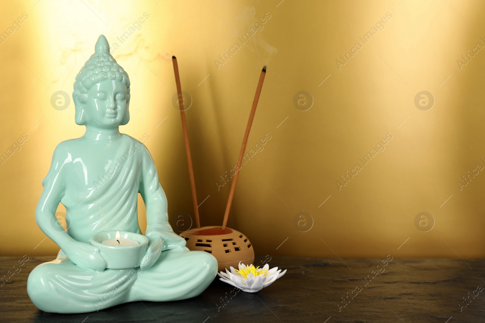 Photo of Buddha statue with burning candle near lotus flower and incense sticks on black table. Space for text
