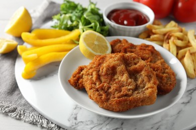 Photo of Tasty schnitzels served with potato fries, ketchup and vegetables on marble board, closeup