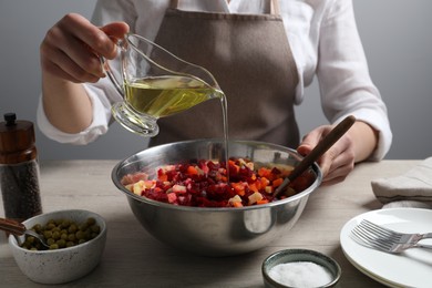 Woman dressing delicious vinaigrette salad at light wooden table, closeup