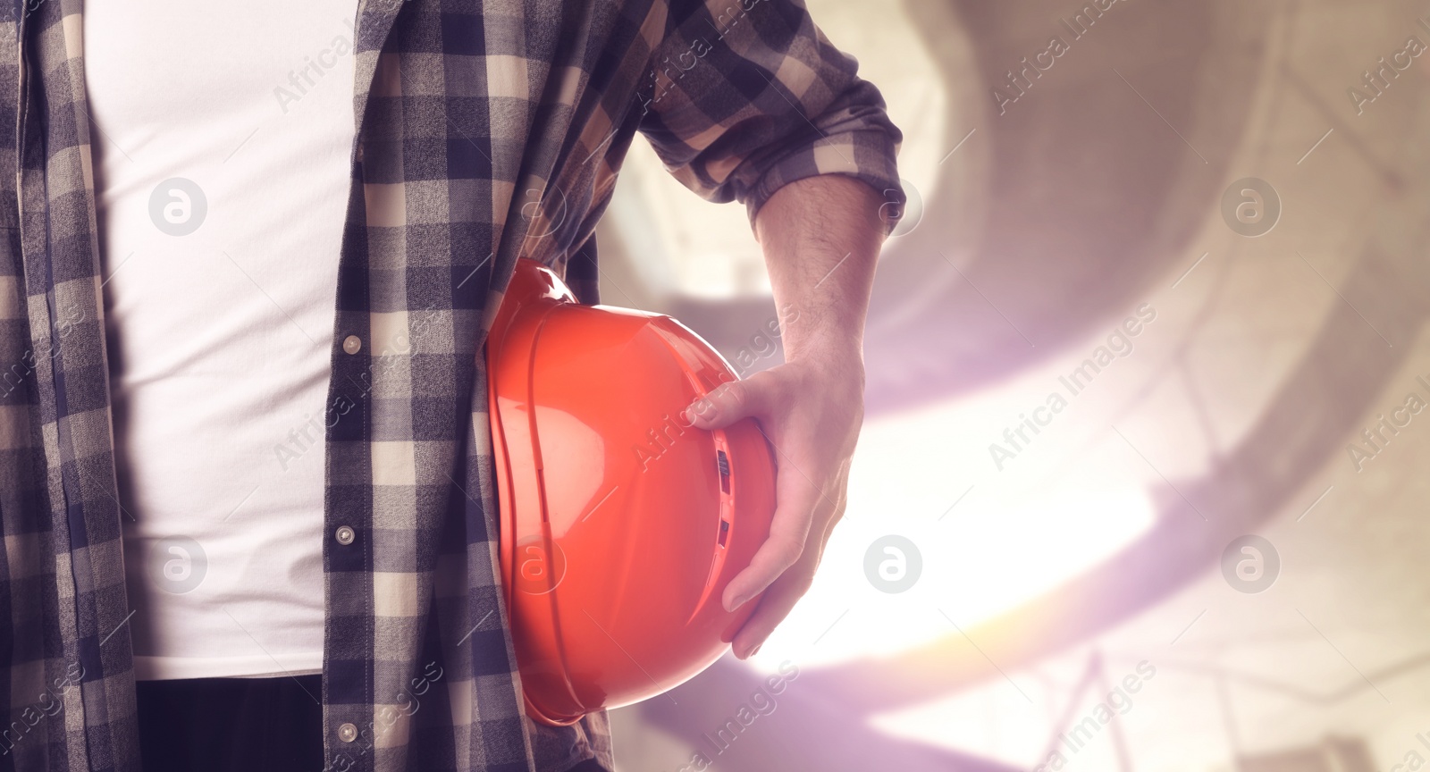 Image of Man with orange hard hat at construction site with unfinished building, closeup. Space for text 