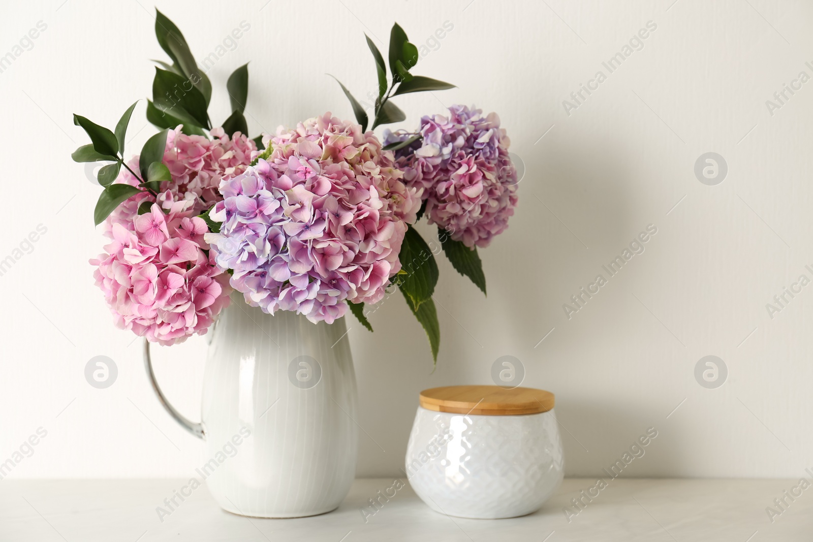 Photo of Bouquet with beautiful purple hydrangea flowers and jar on light countertop
