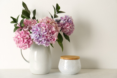 Bouquet with beautiful purple hydrangea flowers and jar on light countertop