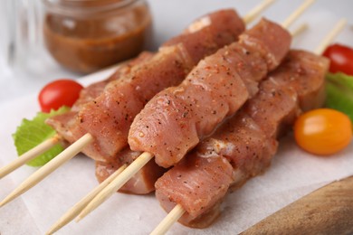 Photo of Wooden skewers with cut raw marinated meat on table, closeup
