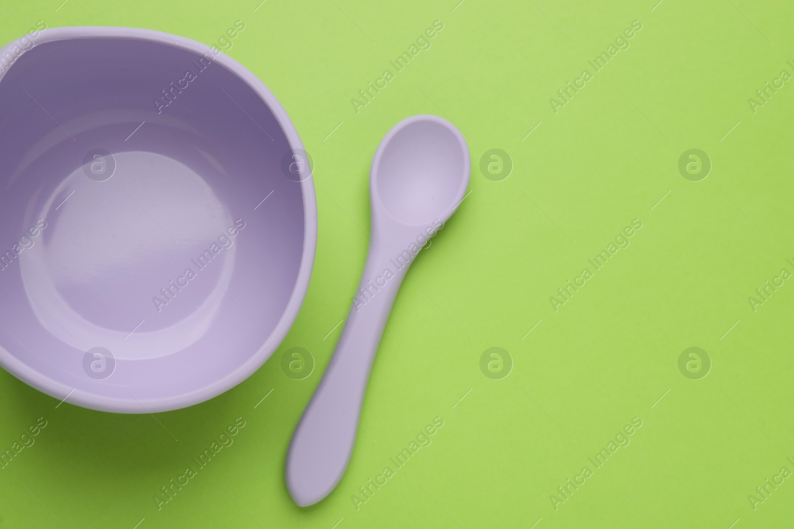 Photo of Plastic bowl and spoon on light green background, flat lay with space for text. Serving baby food